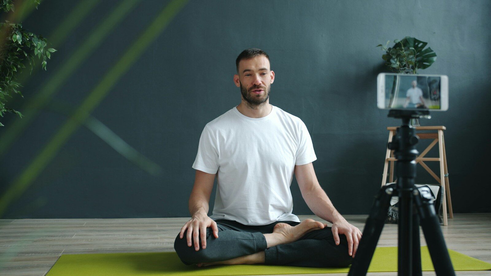 Man meditating on yoga mat recording with phone